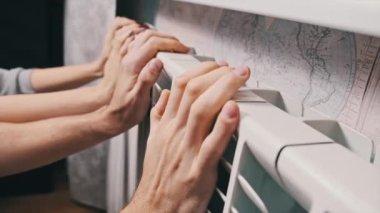 Donmuş erkek ve kadın elleri radyatöre dokunup ısınmaya çalışıyor. Ev ısıtma problemi. Soğuk mevsim konsepti sırasında ev sıcaklığı. Elleri ısıtma pili ile ısıtılır. Apartman soğuk.
