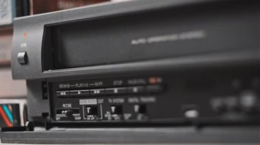 Male hand inserts VHS cassette into a VCR Video recorder. Black vintage videotape cassette recorder on desk with many video cassettes. Inserting retro VHS tape into vintage player. Home video archive
