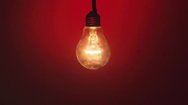 Koyu kırmızı arka planda parlak ve yanıp sönen lamba. Edison ampulü yavaşça açılıp kapanıyordu. Yakından yanıp sönüyordu. Ilık yanıp sönen filament. Retro klasik ampul. Uzaklaştır