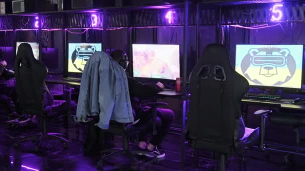 十代の友人は コンピュータクラブでオンラインゲームをプレイします Pc上でシューティングゲームをプレイイヤホン付きのコンピュータ椅子の男の子 ネオンのクラブでゲームルームで遊んでいるゲーマー — ストック動画
