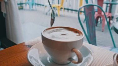 Sokak manzarasının karşısındaki kafeteryada köpüklü bir bardak kapuçino. Eski şehrin penceresine bakan sıcak bir kafe atmosferi var. Kahve fincanına yakın çekim. Kahve dükkanında birini bekliyorum..