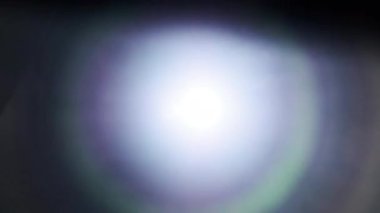 The light of a bright flashlight directed at the camera moves from side to side. Light effect of reflections in lenses. Flashes of blue light, effect. Transition, lens flare, light leaks. 4K