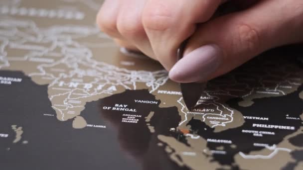 スクラッチワールドマップの表面にタイ国をスクラッチ 女性の手の消去旅行マップ上の国を訪問した 多くの国とスクラッチ世界地図 クローズアップ 企画旅行の概念 — ストック動画