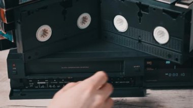 Erkek eli, eski bir video kayıt cihazından VHS çekiyor. Arşivlenmiş video kasetlerin olduğu bir masadaki bir video oynatıcıdan VHS kaseti çıkar. VHS retro oynatıcı. Ev videosu kavramı, eski teknoloji