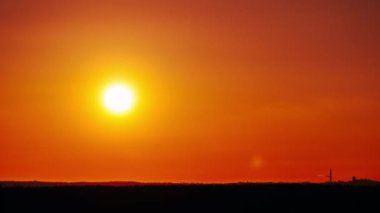 Timelapse of sunset in the orange sky over the horizon. Big bright red sun with sunrays moves down in a light evening haze. Awesome epic cloud space, vibrant color. Time Lapse. Sundown. 4K