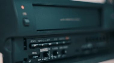 Insert VHS cassette into VCR player. Black vintage videotape cassette recorder on a desk with many archived video cassettes. Male hand inserting old VHS Tape into a retro player. Home video, nostalgia
