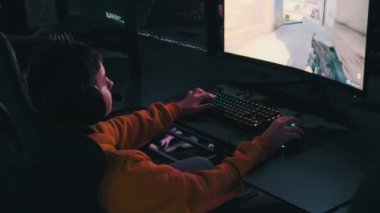 Bilgisayar kulübündeki bir çocuk oyun sandalyesinde oturup atış oyunu oynuyor. Esport Siber Kulübü 'nde kulaklık takan ve neon ışıkları video oyununa odaklanan bir genç. E-spor, hobi, sanal turnuva