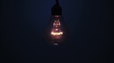 Incandescent lamp glows and flickers on dark blue background. Edison light bulb slowly turned on and off, pulsing light close-up. Warm flashing filament. Retro classic bulb. Copy space, place for text