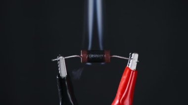 The resistor heats up with smoke under a high current strength, short circuit. An electrical component in lab burns out when exposed to high voltage. Close-up, resistance. Electric power, Ohms law.
