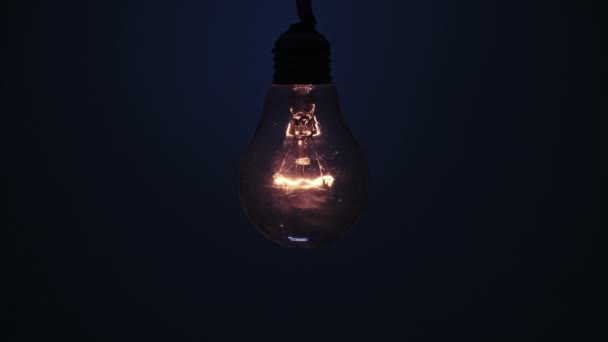 白熱灯は濃い青の背景に輝き ちらつきます エジソン電球がゆっくりとオンとオフになり ライトが閉まりました 暖かい点滅フィラメント レトロな古典的な電球 コピースペース テキストの場所 — ストック動画