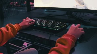Esport kulübünde genç bir çocuk monitörün önünde oturur ve bir nişancı oyunu oynar. PC klavyesinde neon ışıkta duran bir çocuğun elleri görülüyor. Modern oyun kulübündeki gençler bilgisayar oyunları oynuyorlar.