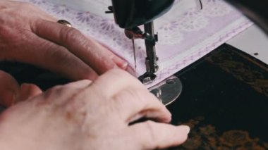 Grandmother sews on vintage sewing machine at home in slow motion. Close-up of the steel sewing machine needle quickly moves up and down. Old female hands of seamstress sewing fabric. Lifestyle, hobby