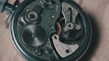 Clock mechanism rotates close-up. Vintage round stopwatch mechanism working in a macro. Old retro clockwork gears, cogwheels, and pendulum movement inside the ancient metal watch.