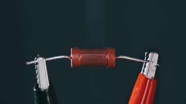 The resistor heats up with smoke under a high electric current, short circuit. Resistor - An electrical component burns out when exposed to high voltage. Close-up, resistance. Current strength, power