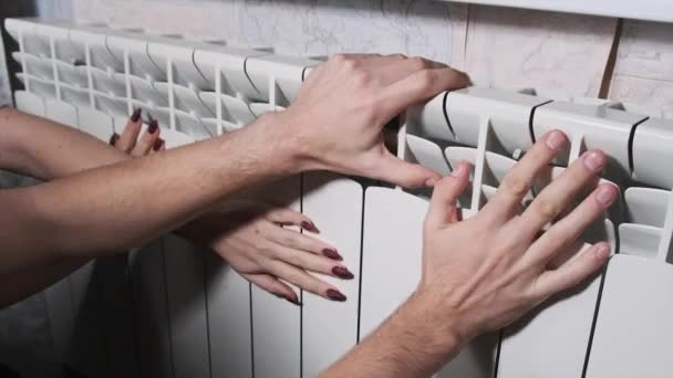 カップルは壁によって暖房ラジエーターの手を暖める 冷凍男性と女性の手は 家庭用加熱バッテリーに触れ 暖かくしようとします 寒い季節に家を加熱する問題 暖房設備が悪い — ストック動画