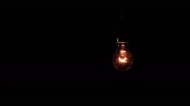 Siyah arka planda yanıp sönen parlak bir ampul açıp kapanıyor ve yanıp sönüyor. Isınan filament yakın plan. Cam gibi parlak sarı bir ampul. Tungsten lamba ışığı. Fikir 4K