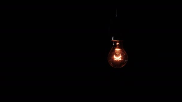 白熱電球がオンになり オフと黒の背景にちらつき テキストのための場所 暖かい点滅フィラメントのクローズアップ ガラス古い電球輝く黄色暖かい光 タングステンランプライト アイデア — ストック動画