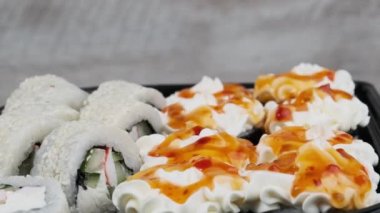Japon suşi ruloları plastik kutuda dönüyor, yakın plan. Zencefilli, wasabi ve soya soslu taze suşi. Philadelphia peynirli suşi, nori, yengeç çubuğu, somon filetosu ve salatalık.