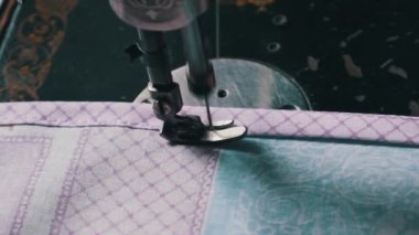 Old female hands of seamstress sew at a retro sewing machine at home in slow motion. Close-up of aged female fingers sewing fabric at a traditional sewing machine. The needle quickly moves up and down
