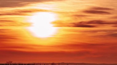 Timelapse of sunset in the orange sky behind the layered clouds over the horizon. Big bright red sun with sunrays moves down. Awesome epic cloud space, vibrant color. Time Lapse. Amazing sundown. 4K
