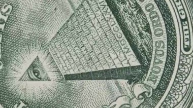 The all-seeing eye sign rotates on a one dollar bill close-up. Mason sign symbol. Concept inflation, economy, conspiracy. US banknote in macro with pyramid and mason eye. New world order, elite.