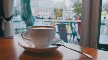 Sokak manzarasının karşısındaki kafeteryada köpüklü bir bardak kapuçino. Eski şehrin penceresine bakan sıcak bir kafe atmosferi var. Kahve fincanına yakın çekim. Kahve dükkanında birini bekliyorum..