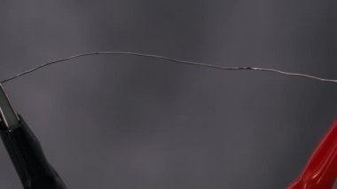 Nichrome wire heated to red under high current strength. Nichrome thread connected to power wires in a lab. Metal filament glowing, high metal resistance, short circuit. Electric power. Close-up
