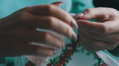 A young woman sews manually with thread and needle in slow motion, close-up. Female fingers with manicures sew while sitting in casual clothes on the sofa at home. Cozy atmosphere, lifestyle, handmade