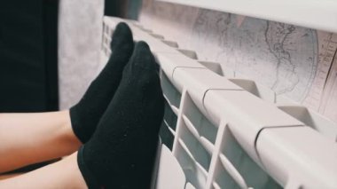 Çoraplı kadın bacakları ısınmak için kalorifere dokunuyor. Kötü ısıtma sistemi kavramı, dairede soğuk kış mevsimi, ısıtma sorunu, merkezi ısıtma. Soğuk biri ısınmaya çalışır.
