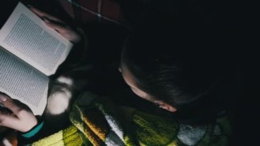 A woman reads a book lying on a sofa at night in the light of a lantern. A female in a dressing gown and cozy room is busy reading. Enjoying a book in a living room. Woman reading during a blackout