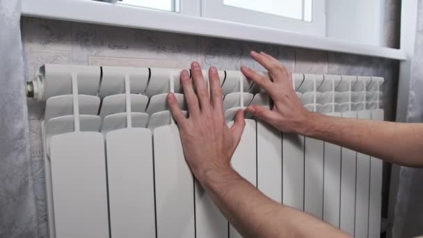 男性の手のひらは壁に対して冷たい加熱ラジエーターに触れる 男の手は家の暖房システムに暖かく保つことを試みている 貧しい暖房システムの概念 アパートで寒い 冬の季節 — ストック動画