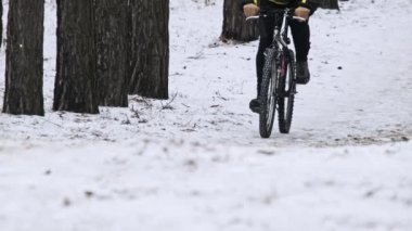 Man ride a bicycle along a snowy path between winter trees in slow motion. Young man biking follows the forest track in woodland. Cyclist travel on bike. Healthy lifestyle, outdoor walking, sport