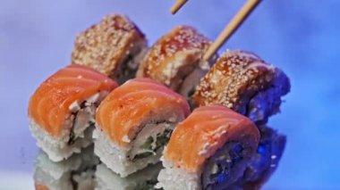 Çubuklar, suşi olarak çubuk kullanarak setten bir suşi rulosu alıyor, yakın plan. Taze Japon unagi suşisi ve somon ve Philadelphia peynirli rulo. Geleneksel deniz ürünleri mutfağı