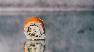 Çubuklu insan eli tut ve bir suşi rulosunu al, yakın plan. Somon balıklı Japon suşisi ve ayna masasında Philadelphia peyniri. Geleneksel deniz ürünleri mutfağı