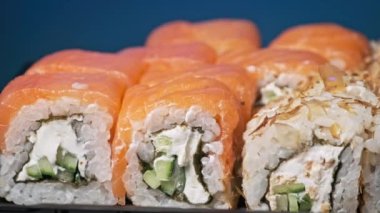Sopalar suşi kutusundan suşi alır, yakın plan. Plastik bir kutuda yuvarlanıyor. Çeşitli lezzetli Japon suşilerinden oluşan hazır yemek seti teslimat konteynerinde. Sağlıklı beslenme, Asya yemekleri, hazır yemek.