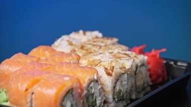 Suşi plastik bir teslimat kutusunda yuvarlanır. Yakın çekim döner. İçinde taze Japon dürümleri, zencefil ve plastik bir kapta dönen wasabi olan suşi kutusu. Yemek teslimatı, paket yemek.