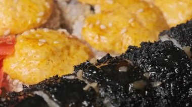 Suşi plastik bir teslimat kutusunda yuvarlanır. Yakın çekim döner. Yemeye hazır suşi kutusu ve farklı pişmiş lezzetli Japon dürümleri plastik kabın içinde dönüyor. Yemek teslimatı, paket yemek.