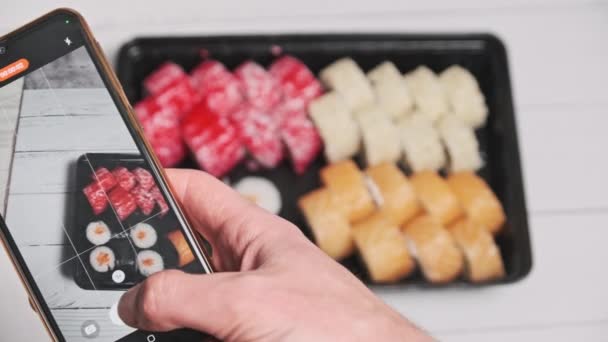ブログでは Snsに投稿するためのスマートフォンカメラで寿司ロールの動画を撮影しています 携帯電話の宅配プラスチック製の箱で日本食を撮影する男性の手 ソーシャルメディアのための撮影 — ストック動画