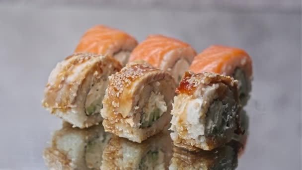 寿司を食欲をそそるミラーテーブルの上に回転します すぐに食べられる日本の寿司ロールがクローズアップされます 新鮮なうなぎ寿司とサーモンとフィラデルフィアチーズのロールのセット — ストック動画
