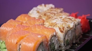 Suşi plastik bir teslimat kutusunda yuvarlanır. Yakın çekim döner. İçinde taze Japon dürümleri, zencefil ve plastik bir kapta dönen wasabi olan suşi kutusu. Yemek teslimatı, paket yemek.
