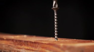 Vidalar tahta tahtaya tornavidayla vidalanmış, yakın plan. Kendi kendini beceren bir vida makro matkapla kendi yerine saplanmış. Tahtayı kesen ipliklerin dönüşü.