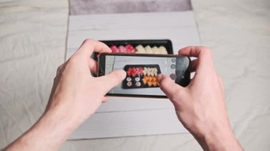 Blogcu sosyal ağlarda paylaşım yapmak için akıllı telefon kamerasıyla suşi rulolarının fotoğrafını çekiyor. Erkek eller, Japon yemeklerini plastik bir kutuda cep telefonuyla çekiyor. Sosyal medya için hazırlanmış çekim.