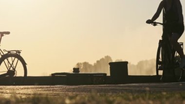 Gün batımında parkta bisiklet süren bir kadının silueti ağır çekimde bisiklet yoluna çıkar. Şehir setinde bisiklet süren bir kız. Hayattan zevk alma kavramı, neşe, sağlıklı yaşam tarzı.