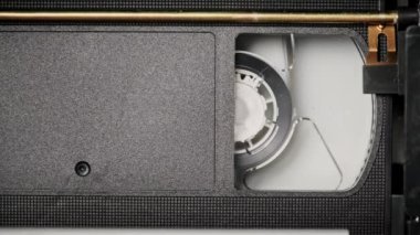 VHS kaset bir VCR kaydedicinin içinde oynatılıyor, üst görünümde. Video kaset makaraları dönüyor. Boş etiketli video kaset oynatmaya başlıyor. İçerideki eski video kaydedici. Eski filmi oynuyorum..