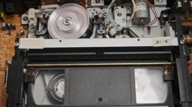 VHS video kasedi VCR kaydedicinin içine koyuldu ve oynatılıyor. Video kasetin klasik VHS mekanizması video başına bant takar. İçerideki eski video kaydedici. Eski video dosyası veya film çalma kavramı.