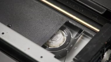VHS kaset bir VCR kaydedicinin içinde oynatılıyor, üst görünümde. Videokaset makaraları dönüyor. Boş etiketli video kaset oynatmaya başlıyor. İçerideki eski video kaydedici. Klasik film oynatılıyor
