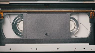 VHS kaset bir VCR kaydedicinin içinde oynatılıyor, üst görünümde. Videokaset makaraları dönüyor. Boş etiketli video kaset oynatmaya başlıyor. İçerideki eski video kaydedici. Klasik film oynatılıyor