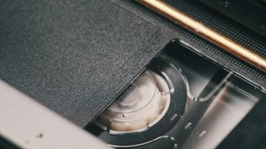 VHS kaset bir VCR kaydedicinin içinde oynatılıyor, üst görünümde. Videokaset makaraları dönüyor. Boş etiketli video kaset oynatmaya başlıyor. İçerideki eski video kaydedici. Klasik film oynatılıyor