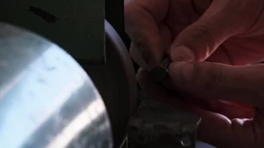 Metal bir parçayı ağır çekimde işlemekten parlak kıvılcımlar çıkıyor. Elektrikli öğütme çarkında metal öğütme, yakın plan. Bir atölyede aşındırıcı bir tekerlek üzerinde çalışan bir zanaatkarın elleri..