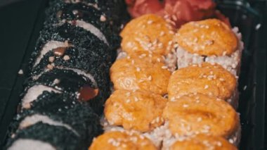 Suşi plastik bir teslimat kutusunda yuvarlanır. Yakın çekim döner. Yemeye hazır suşi kutusu ve farklı pişmiş lezzetli Japon dürümleri plastik kabın içinde dönüyor. Yemek teslimatı, paket yemek.